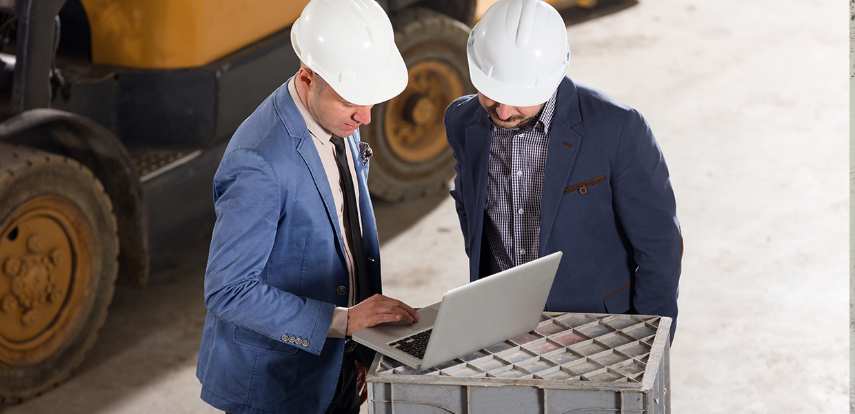 Business men in front of forklift looking at a laptop